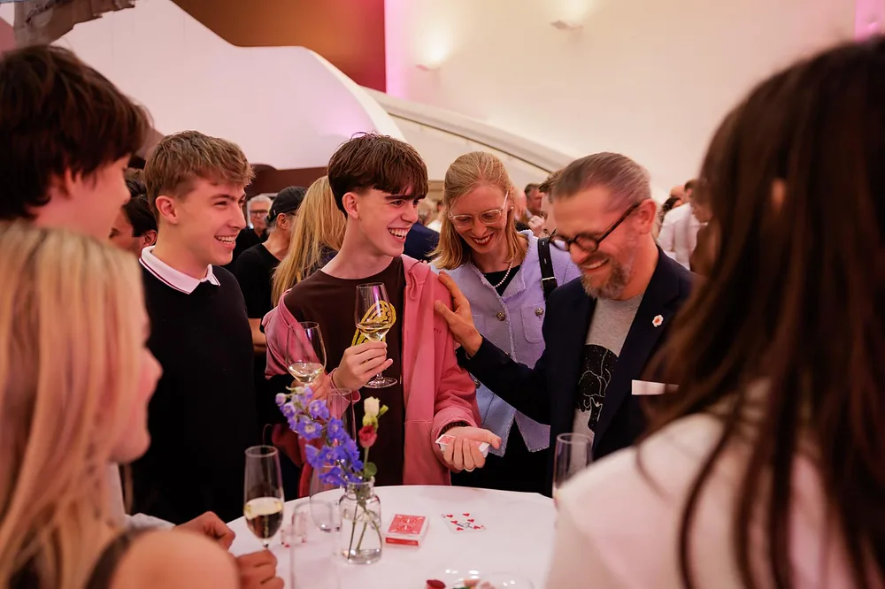 Close-Up Zauberei am Stehtisch: Gäste lachen und staunen, ein Gast hält die Spielkarte selbst in der Hand – Zauberer Simabu