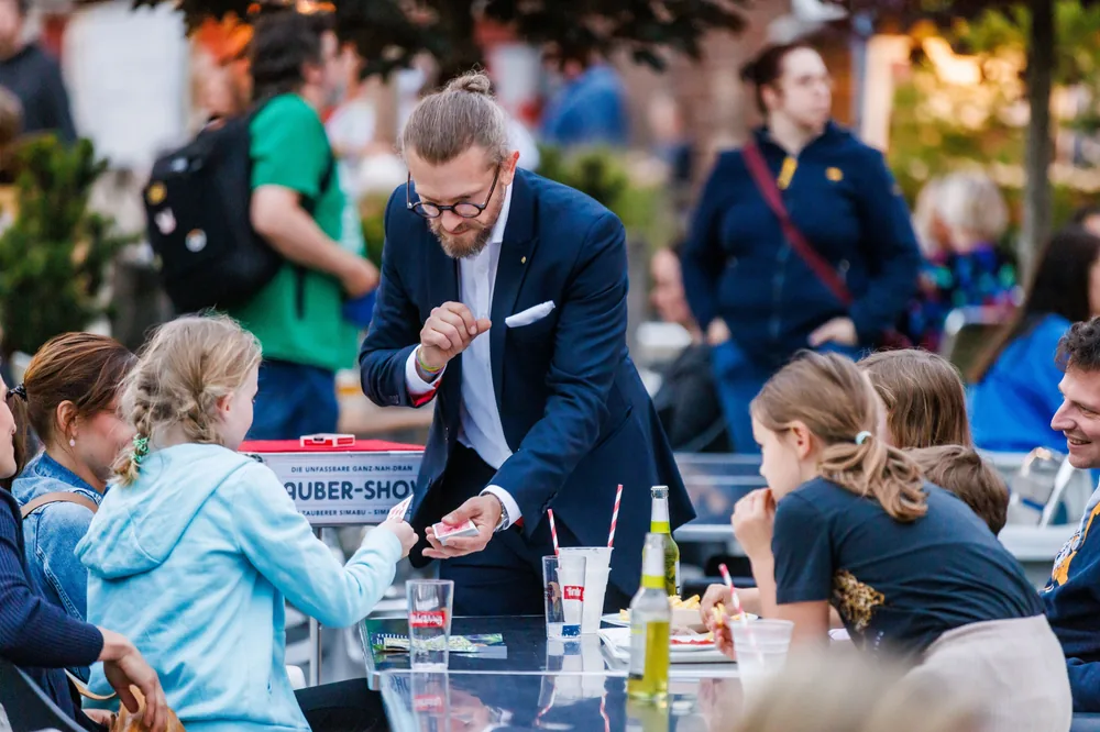 Familienfeier im Freien: Zauberer Simabu am Tisch mit Kindern und Erwachsenen