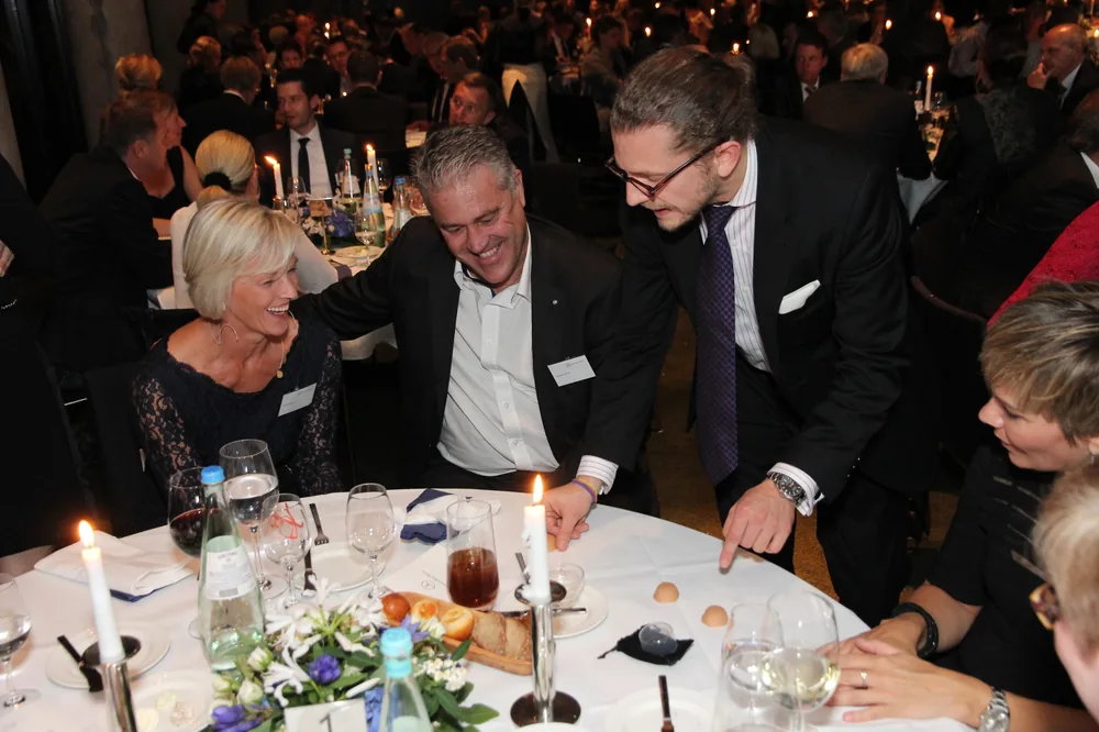Close-Up Walk-Act – Simabu Zauberer Simabu am Tisch einer Firmenfeier – Gäste beugen sich staunend über die Karten